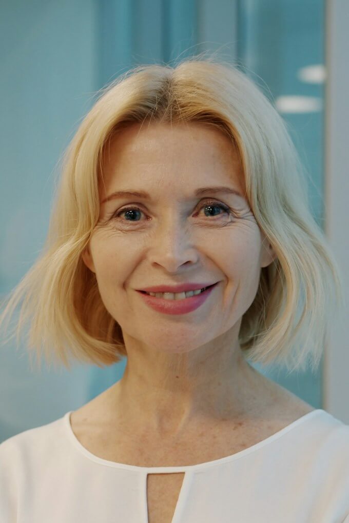 Leende äldre kvinna med blond page, ljust företagsporträtt
