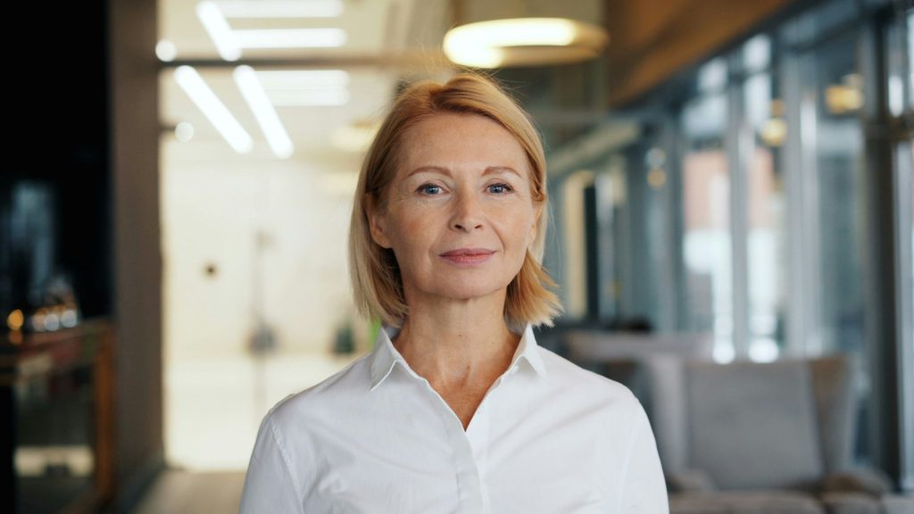 Headshot av kvinna med ljust hår i vit skjorta på ett kontor